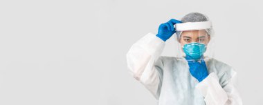 Covid-19, koronavirüs hastalığı, sağlık çalışanları konsepti. Ciddi görünümlü Asyalı kadın doktor, yüz kalkanı ve solunum cihazını tak, kişisel koruyucu ekipman, beyaz arka plan.