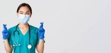 Covid-19, koronavirüs hastalığı, sağlık çalışanları konsepti. Umut dolu Asyalı doktor. Maskeli ve eldivenli. Sol üst köşeye bakıyor ve dua ediyor.