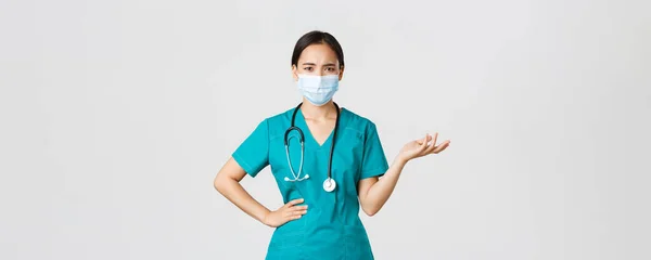 Covid-19, choroba koronawirusowa, koncepcja pracowników służby zdrowia. Zdezorientowany i zdenerwowany azjatycki lekarz w masce medycznej i peelingu, podnieść rękę do góry zastanawiające, nie mogę zrozumieć, jaki problem, białe tło — Zdjęcie stockowe