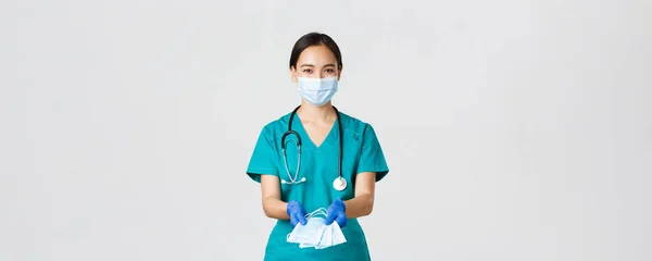 Covid-19, koronavírus betegség, egészségügyi dolgozók koncepciója. Barátságos mosolygós ázsiai orvos, női orvos köpenyben és gumikesztyűben átadja orvosi maszkokat a betegeknek, fehér háttér — Stock Fotó