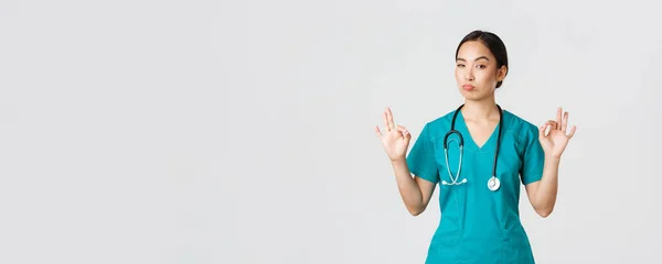 Ковід-19, медичні працівники, пандемія. Вражена привабливою азіатською медсестрою в скрабах, лікар показує нормальний жест і вузол в схваленні, хвалити відмінний вибір, компліментувати когось — стокове фото