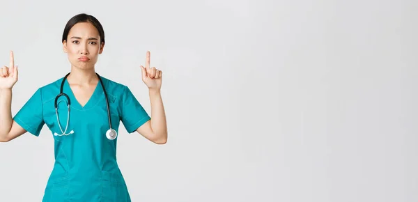 Covid-19, sağlık çalışanları, salgın konsepti. Hüzünlü Asyalı kadın doktor, önlüklü doktor parmaklarını kaldırıyor ve yüzünü buruşturuyor, beyaz arka planda duruyor. — Stok fotoğraf
