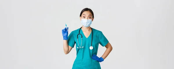 Covid-19, coronavirus ziekte, gezondheidswerkers concept. Amusant lachende Aziatische arts, vrouwelijke arts met medisch masker en rubberen handschoenen, bereide spuit met vaccin voor injectie, witte achtergrond — Stockfoto