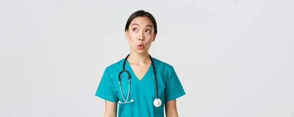 Медичні працівники, запобігання вірусу, концепція карантинної кампанії. Вражена і вражена азіатська жінка-лікар, медсестра в медичних скрабах виглядає верхній лівий кут задоволений, білий фон — стокове фото