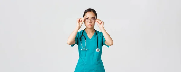 Covid-19, pracownicy służby zdrowia, koncepcja pandemii. Pewna siebie, poważnie wyglądająca i zdeterminowana azjatycka lekarka, pielęgniarka w fartuchu ubrana w okulary, gotowa na zmianę na ostrym dyżurze, białe tło — Zdjęcie stockowe