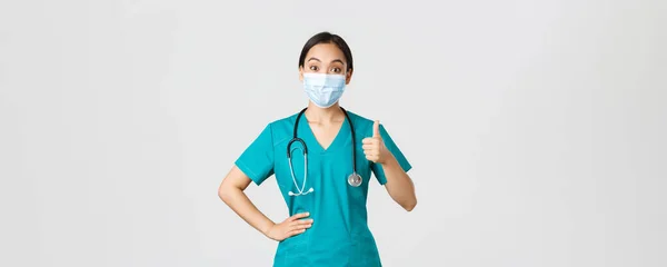 Covid-19, coronavirus disease, healthcare workers concept.给亚洲女医生带来欢乐和印象深刻的是，穿着洗涤剂和医疗面罩的护士，在赞成、同意或称赞他人的工作中表现出大拇指向上 — 图库照片