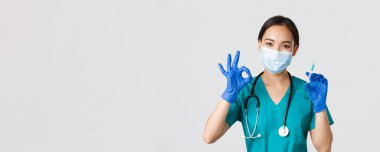 Covid-19, koronavirüs hastalığı, sağlık çalışanları konsepti. Yakışıklı Asyalı kadın doktor, tıbbi maske ve lastik eldiven giyen doktor iyi niyet göstergesi ve aşı ile şırınga, beyaz arka plan