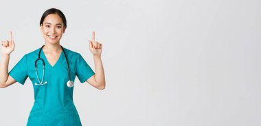 Covid-19, sağlık çalışanları, salgın konsepti. Mutlu gülümseyen Asyalı kadın doktor, önlüklü hemşire ilan veriyor, duyuru yapıyor. Doktorun işaret ettiği pankart