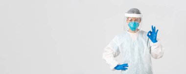 Covid-19, koronavirüs hastalığı, sağlık çalışanları konsepti. Kişisel koruma ekipmanları içinde ciddi görünümlü Asyalı kadın doktor, iyi bir jest gösteriyor, hastanın güvenliğini sağlıyor.