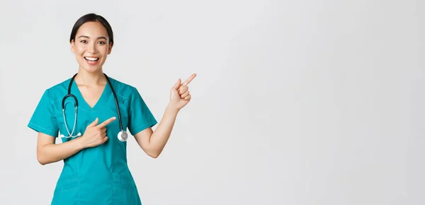 Covid-19, sağlık çalışanları, salgın konsepti. Gülümseyen Asyalı kadın doktor, önlüklü terapist sağ üst köşeyi işaret ediyor, check-up 'a davet ediyor, aşı öneriyor. — Stok fotoğraf