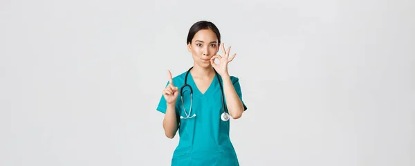 Covid-19, egészségügyi dolgozók, világjárvány. Súlyos kinézetű aggódó ázsiai női nővér, orvos kéri tartsa titokban, remegő ujj és mutatja száj pecsét, cipzár ajkak gesztus — Stock Fotó