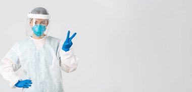 Covid-19, koronavirüs hastalığı, sağlık çalışanları konsepti. Küstah Asyalı kadın doktor, doktor ya da teknoloji laboratuarı kişisel koruma ekipmanları barış işareti gösteriyor, beyaz arka plan