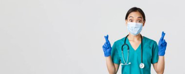 Covid-19, koronavirüs hastalığı, sağlık çalışanları konsepti. Heyecanlı ve umut dolu Asyalı doktor, sağlık maskeli hemşire ve lastik eldiven şans dileyin, dileğinizi gerçekleştirin, beyaz arka plan