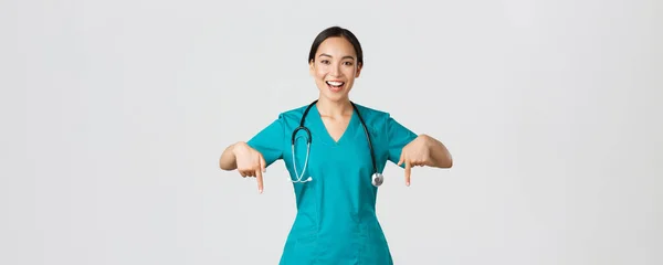 Covid-19, pracownicy służby zdrowia, koncepcja pandemii. Happy uśmiechnięta piękna azjatycka pielęgniarka, lekarz w fartuchu wskazując w dół, zapraszając do badania, pokazując reklamę szpitala, białe tło — Zdjęcie stockowe