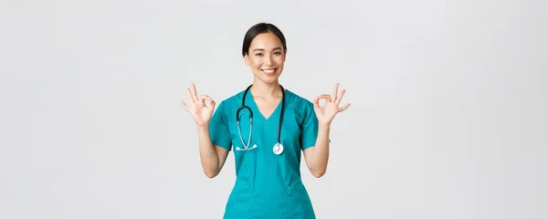Covid-19, trabajadores de la salud, concepto pandémico. Profesional confiado médico asiático mujer, pasante en matorrales asegurar a los pacientes todo lo bueno, mostrando gesto bien satisfecho, sonriendo complacido — Foto de Stock