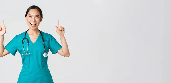 Covid-19，保健工作者，大流行病概念。亚洲快乐的女护士、医生或外科医生，手指头尖着，满意地抬起头，站在苍白的背景上 — 图库照片