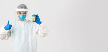 Covid-19, koronavirüs hastalığı, sağlık çalışanları konsepti. Ciddi görünümlü bir laboratuar çalışanı, kişisel koruyucu ekipman araştırmacısı idrar tahlilleri, onaylanmış parmak izleri.