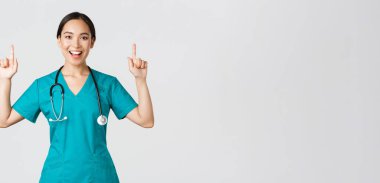 Covid-19, sağlık çalışanları, salgın konsepti. Gülümseyen güzel hemşire, doktor ya da doktor ya da stajyer doktor. Parmakla işaret ediyor, afişi gösteriyor, duyuru yapıyor, reklam yapıyor.