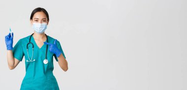 Covid-19, koronavirüs hastalığı, sağlık çalışanları konsepti. Dost canlısı Asyalı kadın doktor, tıbbi maskeli doktor ve şırıngayı aşıyla gösteren önlük.