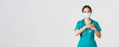 Covid-19, koronavirüs hastalığı, sağlık çalışanları konsepti. Dost canlısı Asyalı kadın doktor, tıbbi maske ve eldiven takmış doktor, kalple el ele tutuşan ve gülümseyen beyaz arka plan.
