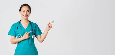 Covid-19, sağlık çalışanları, salgın konsepti. Gülümseyen güzel Asyalı kadın hemşire, sağ üst köşeyi gösteren stajyer doktor, check-up için davetiye, online klinik randevusu, beyaz arka plan