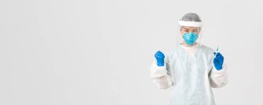 Covid-19, koronavirüs hastalığı, sağlık çalışanları konsepti. Kararlı ve kendinden emin Asyalı kadın doktor, teknoloji laboratuarı çalışanı kişisel koruyucu ekipman elinde aşı şırıngası tutuyor.