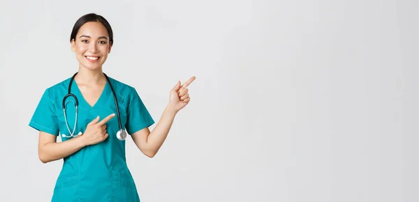 Covid-19, profissionais de saúde, conceito pandémico. Sorrindo bela asiática enfermeira feminina, estagiária apontando dedos canto superior direito, convidando para check-up, consulta clínica on-line, fundo branco — Fotografia de Stock