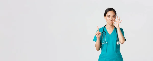 Covid-19, sjukvårdspersonal, pandemikoncept. Allvarligt oroliga asiatiska kvinnliga sjuksköterska, läkare frågar hålla hemligt, skakar finger och visar mun tätning, zippande läppar gest — Stockfoto