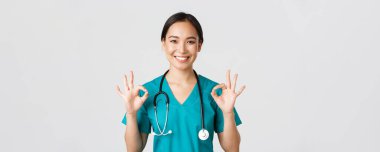 Sağlık çalışanları, virüsü önleme, karantina kampanyası konsepti. Tatmin olmuş yakışıklı Asyalı hemşire, doktor onaylı jest gösteriyor, mükemmel hizmeti öneriyor ya da garanti ediyor.