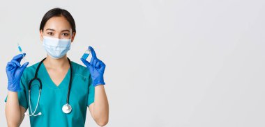 Covid-19, koronavirüs hastalığı, sağlık çalışanları konsepti. Yakışıklı, gülümseyen Asyalı kadın hemşire, aşı ampul ve şırınga gösteren doktor, enjeksiyona hazır olun, beyaz arka plan.