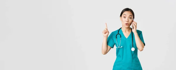 Covid-19, 의료 종사자 및 바이러스 개념 방지. 아름다운 아시아인 여성 의사의 모습, 수술복을 입고 전화 통화를 하는 간호사, 좋은 생각이라고 생각되는 손가락을 들어 올려 계획을 제안하는 것 — 스톡 사진