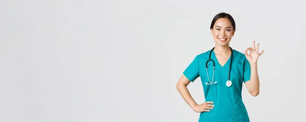 Covid-19, egészségügyi dolgozók, világjárvány. Szakmai magabiztos mosolygós ázsiai nő orvos, női ápolónő köpenyben biztosít mindent ellenőrzés alatt, mutatja rendben gesztus elégedett — Stock Fotó