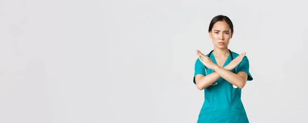 Covid-19, zdravotníci, pandemický koncept. Znepokojený vážně vypadající asijské ženy lékař ukázat křížové gesto, chcete zastavit, zakázat nebo zakázat nebezpečné akce, bílé pozadí — Stock fotografie