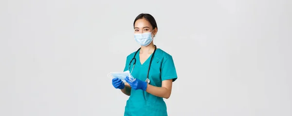 Covid-19, coronavirus sjukdom, vårdpersonal koncept. Leende vänliga kvinnliga sjuksköterska, läkare i skrubb och gummihandskar ger patienter med medicinska masker, vit bakgrund — Stockfoto