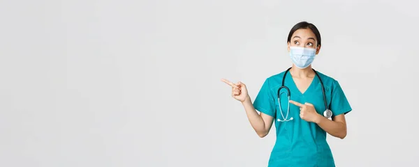 Covid-19, onemocnění koronavirem, koncept zdravotnických pracovníků. vzrušený a ohromený asijský lékař, lékař v lékařské masce a rukavicích, ukazující prsty v levém horním rohu, bílé pozadí — Stock fotografie