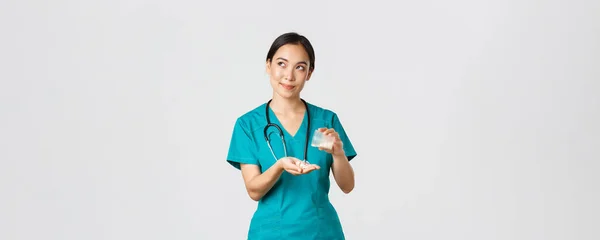 Sjukvårdspersonal, förebyggande av virus, karantänkampanjkoncept. Tankeväckande och omtänksam leende asiatisk kvinnlig sjuksköterska, praktikant i skrubb hantera medicinering till patienten och ser drömska övre vänstra hörnet — Stockfoto