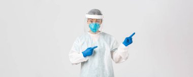 Covid-19, koronavirüs hastalığı, sağlık çalışanları konsepti. Şaşırmış ve şaşırmış Asyalı kadın doktor, kişisel koruma ekipmanları içinde teknoloji laboratuarı çalışanı şaşırmış ve parmağıyla işaret ediyor.