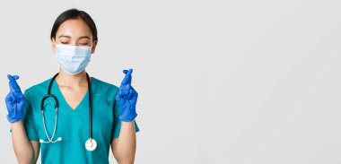 Covid-19, koronavirüs hastalığı, sağlık çalışanları konsepti. Umut verici Asyalı kadın doktor, tıbbi maske ve lastik eldiven giyen doktor, dilek tutuyor, şans diliyor.