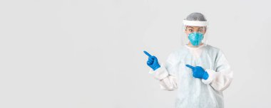 Covid-19, koronavirüs hastalığı, sağlık çalışanları konsepti. Şaşırmış kadın Asyalı doktor, tıbbi solunum cihazı hekimi ve sol üst köşeyi gösteren kişisel koruyucu ekipman.