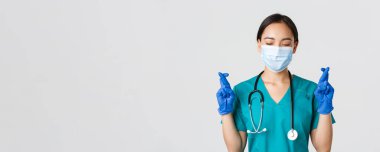 Covid-19, koronavirüs hastalığı, sağlık çalışanları konsepti. Umut verici Asyalı kadın doktor, tıbbi maske ve lastik eldiven giyen doktor, dilek tutuyor, şans diliyor.