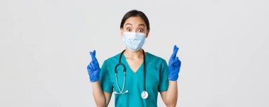 Covid-19, koronavirüs hastalığı, sağlık çalışanları konsepti. Heyecanlı ve umut dolu Asyalı doktor, sağlık maskeli hemşire ve lastik eldiven şans dileyin, dileğinizi gerçekleştirin, beyaz arka plan