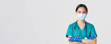 Covid-19, koronavirüs hastalığı, sağlık çalışanları konsepti. Kendine güvenen, gülümseyen, profesyonel Asyalı doktor, tıbbi maskeli hemşire ve lastik eldivenler muayene için hazır, beyaz arka plan.