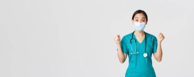 Covid-19, koronavirüs hastalığı, sağlık çalışanları konsepti. Neşeli Asyalı kadın doktor, tıbbi maske ve önlüklü doktor, neşeli görün, sevinç içinde, yaşasın, beyaz arka plan de.