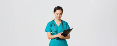 Sağlık çalışanları, virüsü önleme, karantina kampanyası konsepti. Ciddi görünümlü kadın doktor, önlüklü hemşire. Dosyaya bilgi yazıyor, hastayı muayene ediyor, beyaz bir geçmişi var.