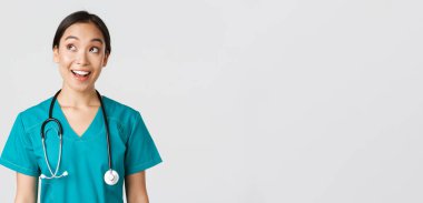 Sağlık çalışanları, virüsü önleme, karantina kampanyası konsepti. Hevesli gülümseyen Asyalı doktor önlüklü, hemşire sol üst köşeye bakıyor, yüzü gülmüş, beyaz arka planda duruyor.