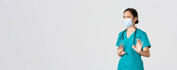 Covid-19, choroba koronawirusowa, koncepcja pracowników służby zdrowia. Niezadowolona azjatycka lekarka, lekarz lub pielęgniarka unikająca kontaktu z zarazkami, nosząca maskę medyczną i fartuch, drżąca odmowa podania rąk — Zdjęcie stockowe