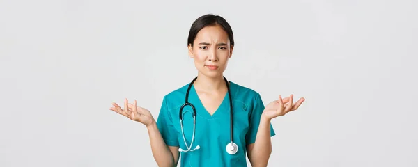 Healthcare workers, preventing virus, quarantine campaign concept. Close-up of confused and puzzled asian female physician in scrubs having complicated problem, raising hands and shrugging — Stock Photo, Image