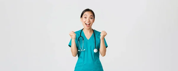 Covid-19, healthcare workers and preventing virus concept. Hopeful and relieved, joyful asian pretty female doctor, physician rejoicing with fists pump, congrats or praise someone, winning — Stock Photo, Image