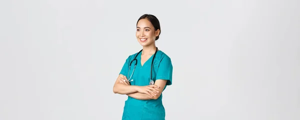 Covid-19, healthcare workers, pandemic concept. Side view of professional confident and hopeful asian female doctor, nurse looking assured away and smiling, standing in scrubs white background — Stock Photo, Image