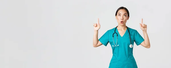 Covid-19, pracownicy służby zdrowia, koncepcja pandemii. Imponujące i fascynujące ładna azjatycka pielęgniarka, lekarz w fartuchu wskazując i patrząc w górę z opuszczoną szczęką, pozostając wow zdumiony — Zdjęcie stockowe